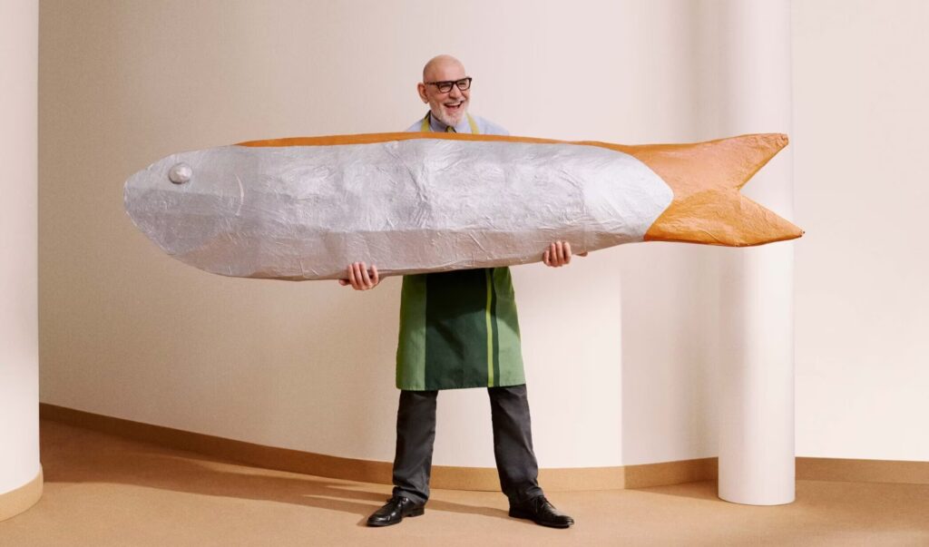 Paolo in a Waitrose uniform holding a giant fake fish and laughing. 