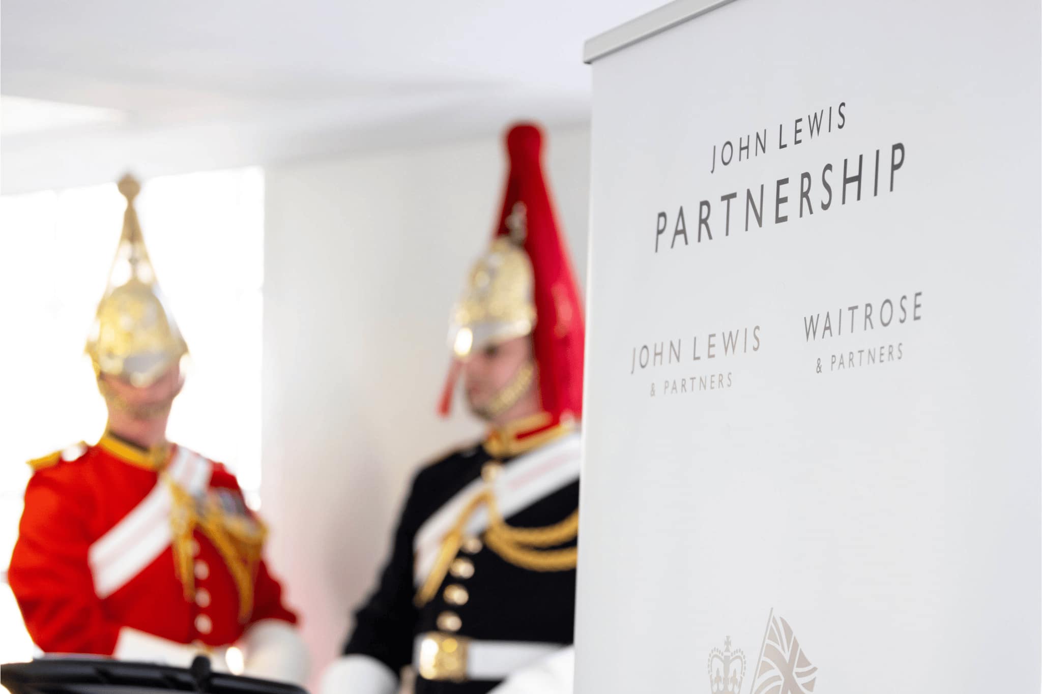 John Lewis Partnership banner in foreground with two men in uniforms in blurred background