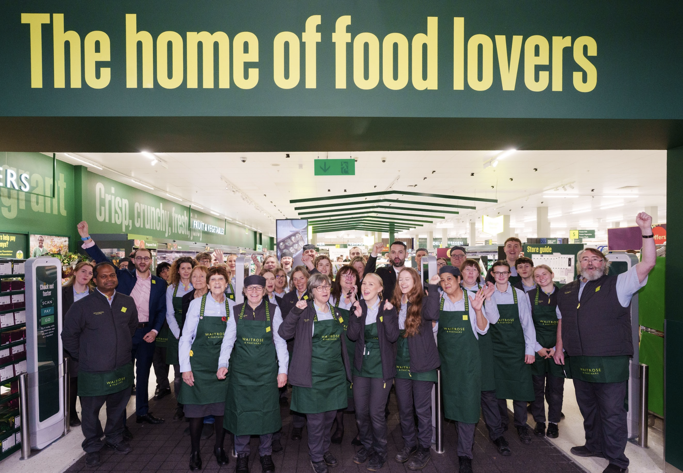 Partners (employees) of Waitrose Newbury stood in the shop entrance below a sign that says 'The Home of Food Lovers'